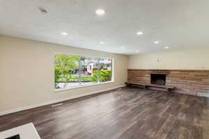 Unfurnished living room with a stone fireplace, recessed lighting, baseboards, and dark wood-type flooring