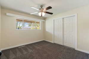 Unfurnished bedroom featuring baseboards, ceiling fan, a closet, and dark colored carpet