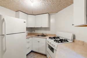 Kitchen featuring a sink, light countertops, white appliances, and white cabinetry