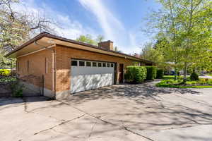 View of property exterior featuring a garage, a chimney, driveway, and brick