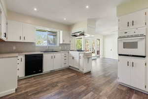 Kitchen with white oven, a sink, dark wood-style floors, black dishwasher, and extractor fan