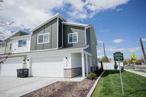 View of property exterior featuring board and batten siding, a lawn, a garage, concrete driveway, and stone siding