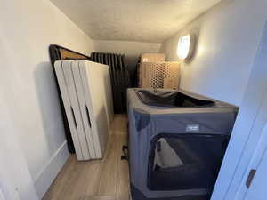Clothes washing area with light wood-type flooring, a textured ceiling, radiator heating unit, and radiator