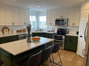 Kitchen with a sink, green cabinetry, stainless steel appliances, and white cabinets