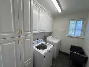 Laundry room with cabinet space, independent washer and dryer, a wainscoted wall, tile walls, and dark tile patterned flooring