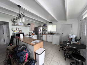 Kitchen with appliances with stainless steel finishes, open shelves, light tile patterned floors, beamed ceiling, and washer / dryer