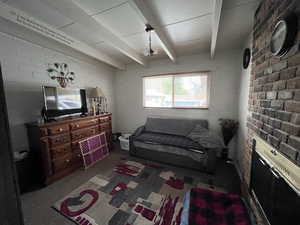 Carpeted living area with brick wall and beamed ceiling