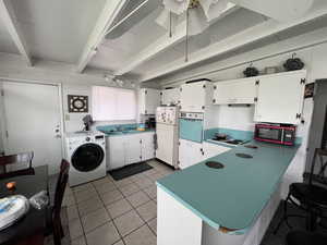 Kitchen featuring freestanding refrigerator, white cabinetry, wall oven, washer / dryer, and beamed ceiling