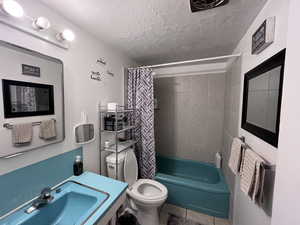 Full bathroom featuring a textured ceiling, tile patterned flooring, shower / tub combo, a sink, and toilet