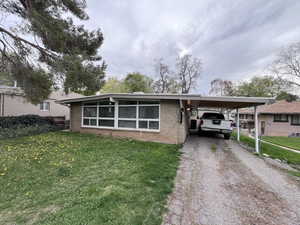 View of front of home with brick siding, a carport, a front lawn, and dirt driveway