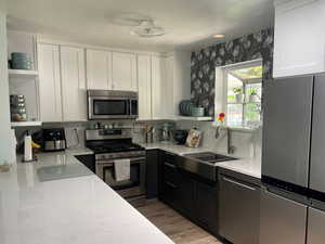 Kitchen with white cabinets, stainless steel appliances, open shelves, and a sink