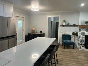 Kitchen featuring light stone countertops, light wood-style floors, a kitchen breakfast bar, freestanding refrigerator, and ornamental molding