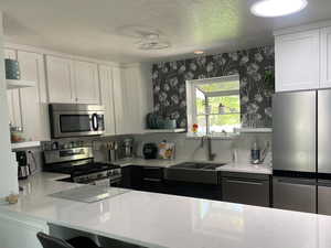 Kitchen featuring a kitchen bar, a sink, white cabinets, stainless steel appliances, and wallpapered walls