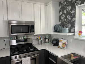 Kitchen featuring appliances with stainless steel finishes, white cabinets, and wallpapered walls