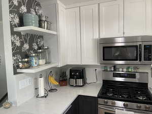 Kitchen with open shelves, light stone countertops, white cabinetry, backsplash, and stainless steel appliances