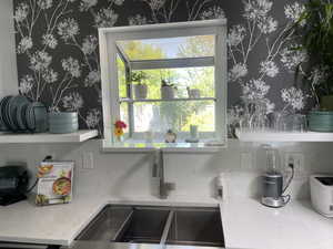 Details with wallpapered walls, light stone counters, and a sink