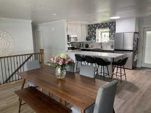 Dining area with crown molding, a wainscoted wall, light wood-type flooring, and a textured ceiling