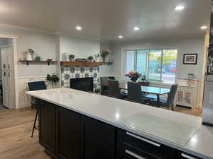 Kitchen featuring a fireplace, dark cabinets, crown molding, and light wood-type flooring