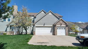 View of front facade featuring a front lawn, stone siding, a garage, stucco siding, and concrete driveway