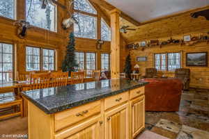 Kitchen featuring wood walls, dark countertops, open floor plan, ceiling fan, and high vaulted ceiling