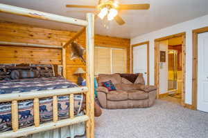 Carpeted bedroom featuring wood walls, connected bathroom, and ceiling fan
