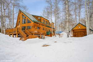 Snow covered rear of property with a wooden deck, log exterior, and metal roof