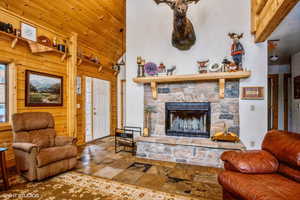 Living area with wood ceiling, a fireplace, wood walls, high vaulted ceiling, and stone tile flooring