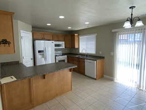 Kitchen with a peninsula, dark countertops, white appliances, a sink, and a notable chandelier