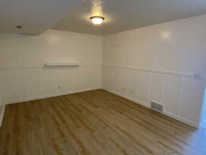 Empty room featuring a decorative wall, wainscoting, wood finished floors, and visible vents