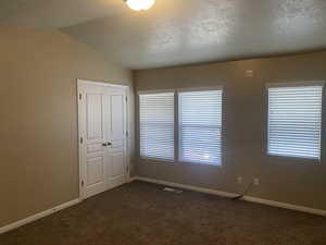 Unfurnished room featuring baseboards, lofted ceiling, dark colored carpet, and visible vents