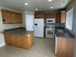 Kitchen with dark countertops, a sink, a peninsula, recessed lighting, and white appliances