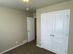 Unfurnished bedroom featuring visible vents, baseboards, dark carpet, and a closet