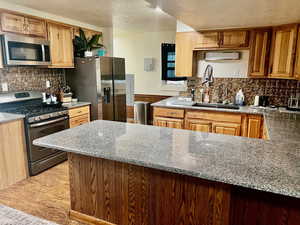 Kitchen with light stone counters, a sink, a textured ceiling, stainless steel appliances, and tasteful backsplash