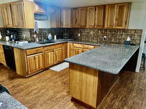 Kitchen featuring a sink, dishwasher, a peninsula, wood finished floors, and backsplash