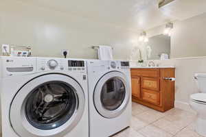 Washroom featuring laundry area, a wainscoted wall, separate washer and dryer, a sink, and light tile patterned floors