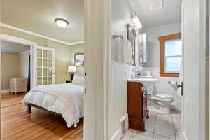 Bedroom with connected bathroom, crown molding, wainscoting, light tile patterned floors, and visible vents