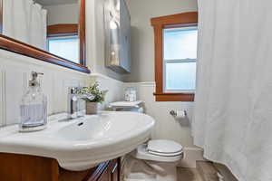 Full bath with a shower with curtain, wainscoting, toilet, and a decorative wall