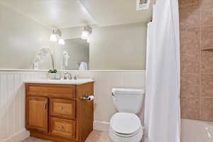 Bathroom with visible vents, vanity, toilet, tile patterned floors, and a wainscoted wall