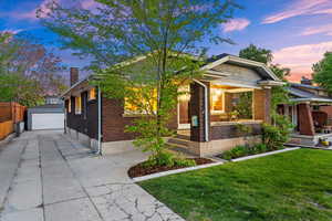 Bungalow-style home featuring a chimney, brick siding, a lawn, an outbuilding, and a detached garage