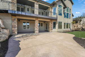 Back of house with stucco siding, a patio area, stone siding, and a balcony
