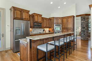 Kitchen with light stone counters, light wood finished floors, stainless steel appliances, decorative columns, and backsplash