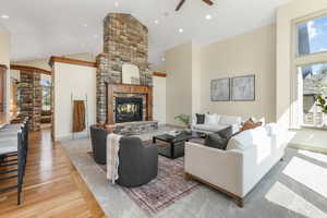 Living room featuring decorative columns, wood finished floors, a fireplace, ceiling fan, and high vaulted ceiling