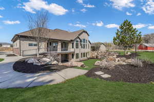Rear view of property featuring a lawn, roof with shingles, stucco siding, and stone siding