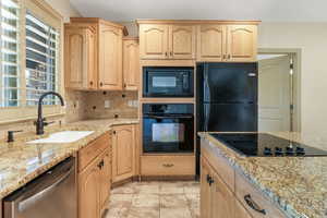 Kitchen with decorative backsplash, light brown cabinetry, light stone countertops, a sink, and black appliances