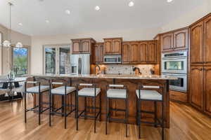 Kitchen with decorative backsplash, a breakfast bar, light stone counters, light wood-style flooring, and stainless steel appliances