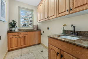 Washroom featuring baseboards, hookup for a washing machine, electric dryer hookup, a sink, and cabinet space