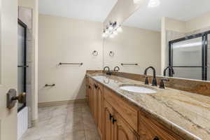 Bathroom featuring double vanity, tile patterned flooring, a sink, and a shower with shower door