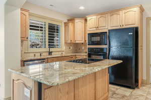 Kitchen with a sink, light brown cabinets, black appliances, and visible vents