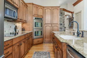 Kitchen with brown cabinetry, backsplash, a sink, light stone counters, and stainless steel appliances