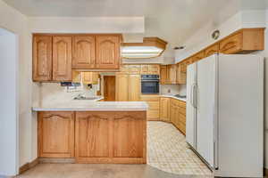 Kitchen with a sink, a peninsula, white appliances, and light countertops